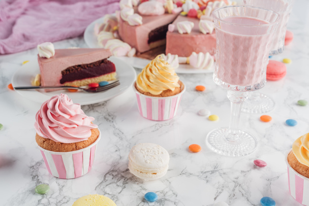 close up of pink cake, marshmallows, candies, sweet cupcakes and milkshake on marble table - Foto, Imagen