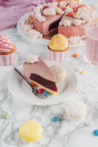 piece of birthday cake, macaroons, colorful cupcakes and milkshake in glass on table  - Фото, зображення