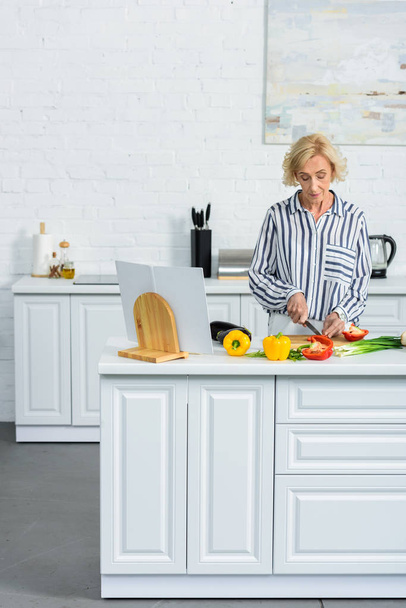 atraktivní šedý vlasy žena vaření v kuchyni a krájení zeleniny - Fotografie, Obrázek