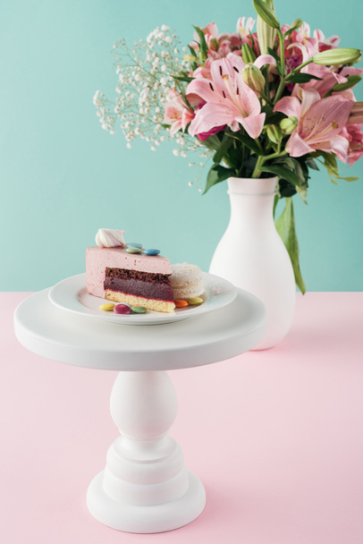 piece of cake with marshmallow and candies on cake stand and bouquet of flowers in vase  - Photo, Image