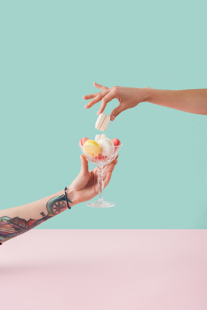 cropped view of woman taking of macaron from glass bowl in tattooed hand - Фото, зображення