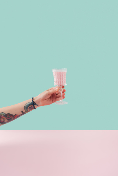 cropped view of female tattooed hand with glass of milkshake on pastel background - Foto, Bild