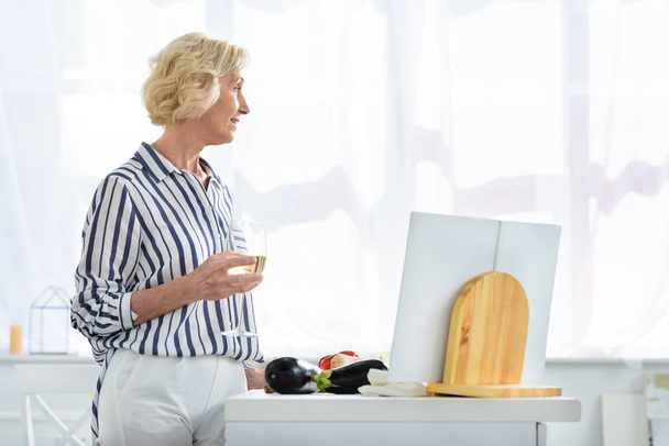 puolella näkymä houkutteleva harmaat hiukset nainen tilalla lasi viiniä keittiössä ja katselee pois
  - Valokuva, kuva