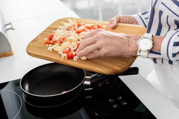 kadın kıdemli koyarak sebze mutfak tava üzerinde resim kırpılmış - Fotoğraf, Görsel