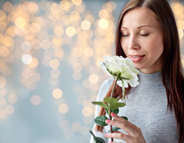 woman smelling white rose over festive lights - Zdjęcie, obraz