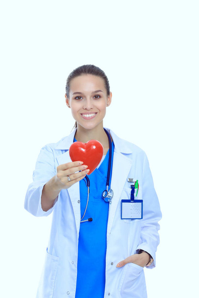 Positieve vrouwelijke arts met de stethoscoop en rood hartsymbool staan geïsoleerd. Vrouw arts - Foto, afbeelding