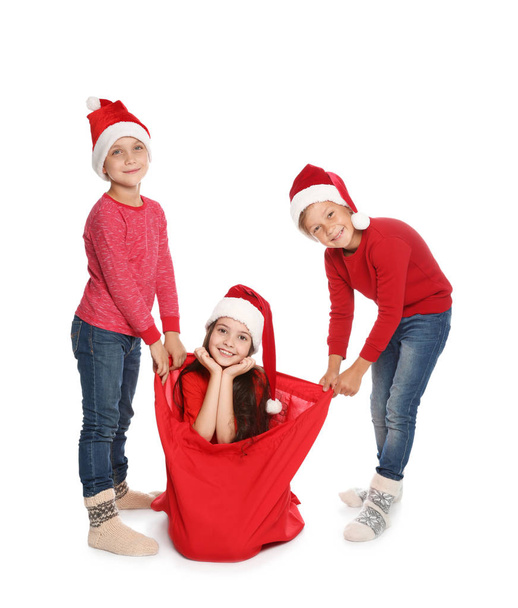 Cute little children in Santa hats with red Christmas bag on white background - Foto, Bild