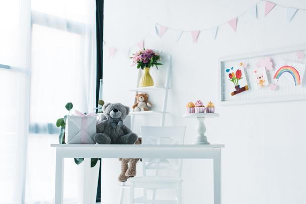 decorado para sala de cumpleaños con oso de peluche, caja de regalo y cupcakes en la mesa
  - Foto, imagen