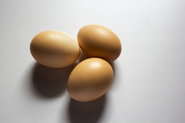 Tres huevos se colocan sobre un fondo blanco y tienen una sombra negra
. - Foto, imagen