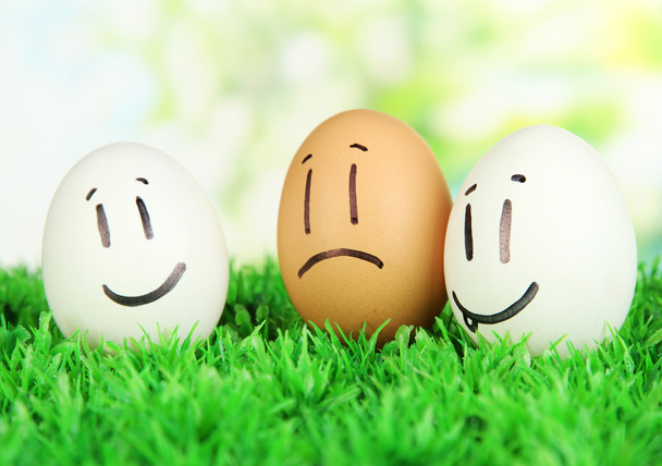 Eggs with funny faces on grass on bright background - Φωτογραφία, εικόνα