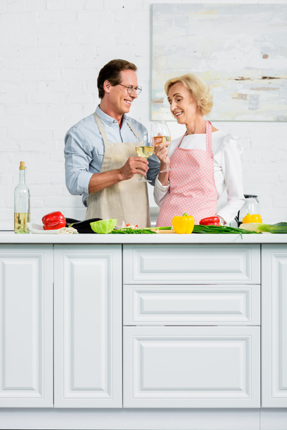 キッチンで調理中にワインのガラスをチリンと幸せな先輩カップル - 写真・画像