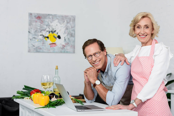 smiling senior couple looking at camera at kitchen - Valokuva, kuva