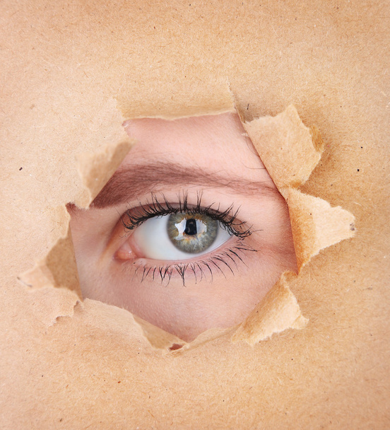 Female eye looking through hole in sheet of paper - Foto, imagen