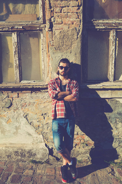 man wearing trendy clothes posing with crossed arms on old house background  - Foto, immagini