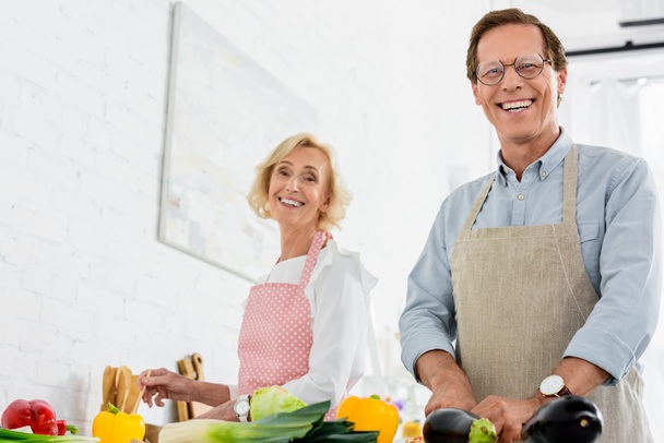 low angle view of happy senior couple cooking together at kitchen and looking at camera - 写真・画像