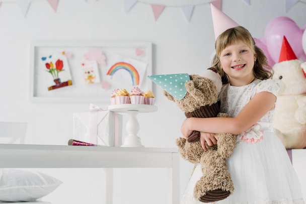 smiling birthday kid holding teddy bear in cone  - Photo, Image