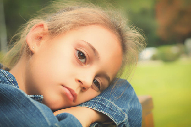 Porträt eines müden kleinen Mädchens in Jeansjacke auf verschwommenem natürlichen Hintergrund  - Foto, Bild