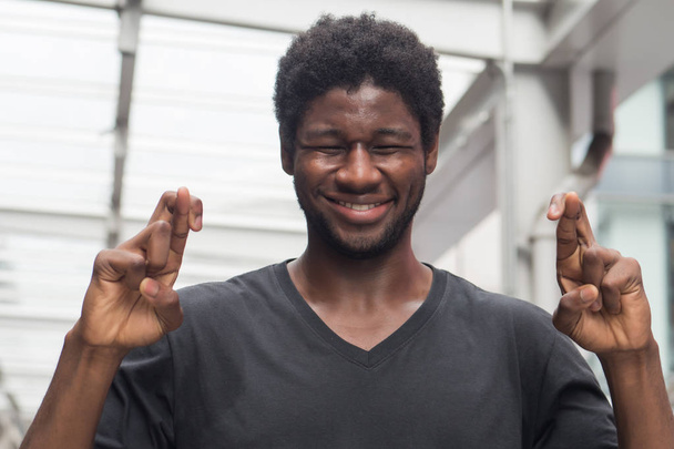 Африканский мужчина скрещивает палец; портрет африканца или черного мужчины со скрещенным пальцем, желающего удачи, загадывающего желание удачи или успеха; африканский молодой мужчина-модель
 - Фото, изображение