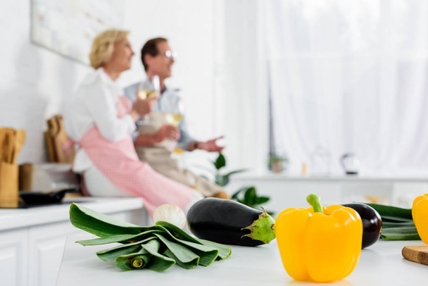 vue rapprochée des légumes frais sur la table de cuisine et du couple de personnes âgées buvant du vin derrière
 - Photo, image