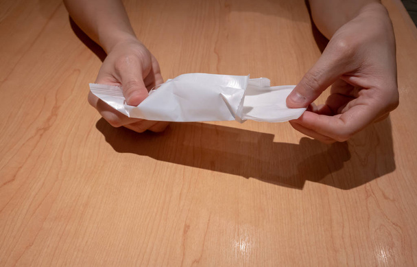 Hand zieht nasses Papier oder Serviette aus Plastikverpackung auf Holztisch - Foto, Bild