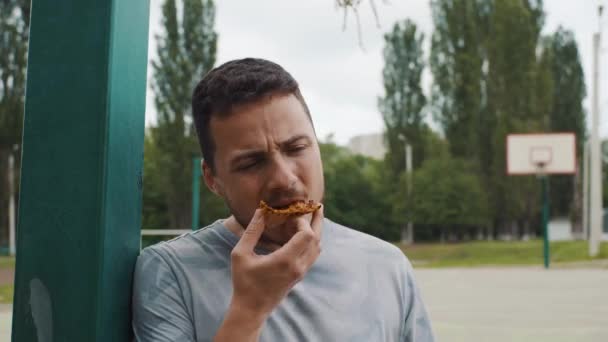 Primer plano del hombre guapo comiendo pizza en una cancha de baloncesto
 - Imágenes, Vídeo