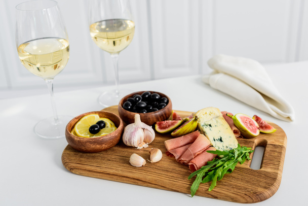 close-up view of delicious snacks on wooden board and glasses of wine on table     - Photo, Image