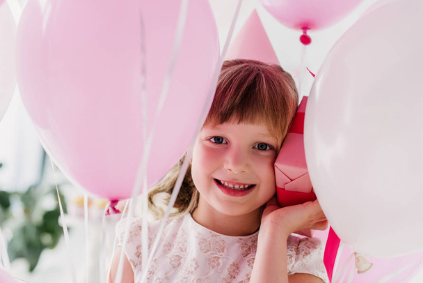 portrait of happy birthday child in cone holding gift box and air balloons  - Fotoğraf, Görsel