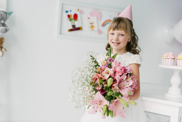 hymyilevä syntymäpäivä lapsi kartio tilalla kimppu liljat
  - Valokuva, kuva