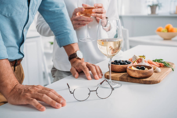 foto recortada de pareja mayor bebiendo vino y comiendo deliciosos bocadillos en casa
  - Foto, imagen