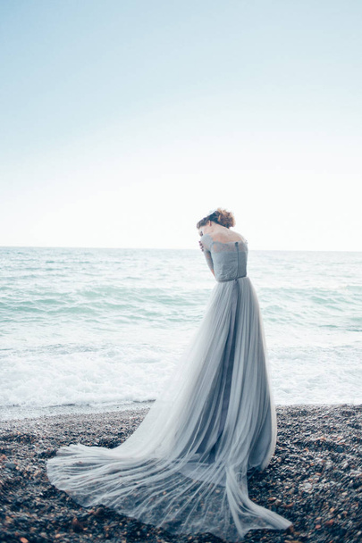 A woman in a long beautiful dress stands near the sea back - Fotoğraf, Görsel