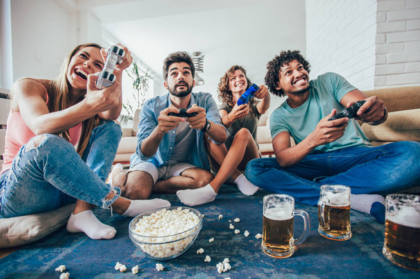Skupina přátel hrát videohry spolu doma a jíst popcorn, baví. - Fotografie, Obrázek