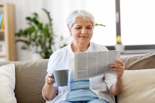 senior woman with coffee reading newspaper at home - Fotografie, Obrázek