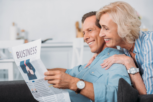 vista lateral do casal de idosos sorridentes ler jornal de negócios em casa
 - Foto, Imagem