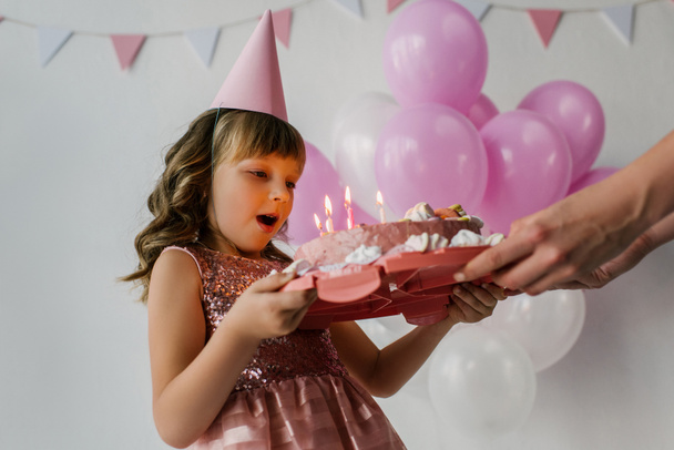 abgeschnittenes Bild von Mutter mit Kuchen, während Geburtstagskind Kerzen auspustet  - Foto, Bild