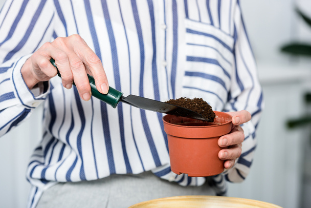 cropped shot of senior woman holding small shovel and pot with soil - 写真・画像