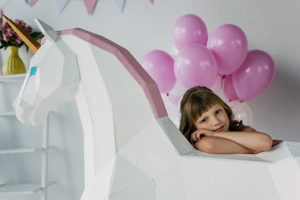 装飾的なユニコーンとピンクの風船の束に座っている小さな子供  - 写真・画像