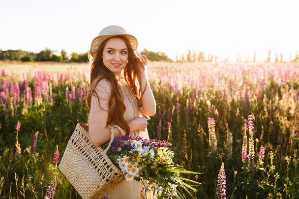 Kobieta spaceru przez lato pole niosąc bukiet kwiatów w torebka - Zdjęcie, obraz