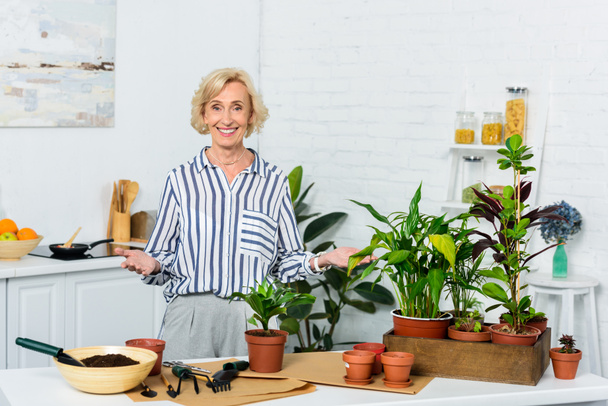 beautiful happy senior woman smiling at camera while cultivating potted plants at home  - Foto, Bild