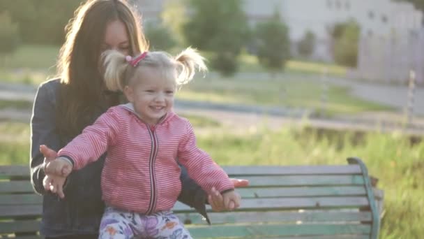 Mom sits on a bench, she has a little girl on her lap. Outside, its a warm spring evening - Footage, Video