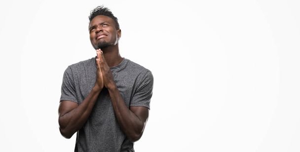 Nuori afrikkalainen amerikkalainen mies yllään harmaa t-paita kerjääminen ja rukoilee kädet yhdessä toivon ilme kasvoillaan hyvin emotionaalinen ja huolissaan. Pyytää anteeksiantoa. Uskonnon käsite
. - Valokuva, kuva
