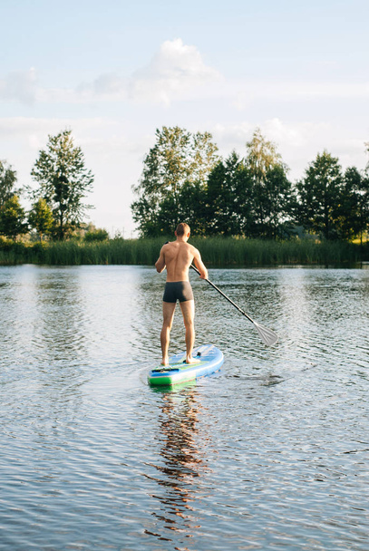 The guy is engaged in paddle boarding on the lake, - Photo, Image