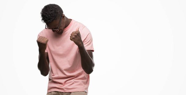 Young african american man wearing pink t-shirt very happy and excited doing winner gesture with arms raised, smiling and screaming for success. Celebration concept. - Valokuva, kuva