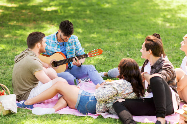 friends playing guitar at picnic in summer park - Фото, изображение