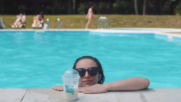 Beautiful young woman swiming in pool and drinking milk shake - Кадри, відео