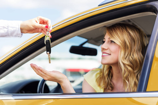 Uma mulher atraente num carro recebe as chaves do carro. Aluguer ou compra de automóvel - conceito. Foco em chaves
. - Foto, Imagem