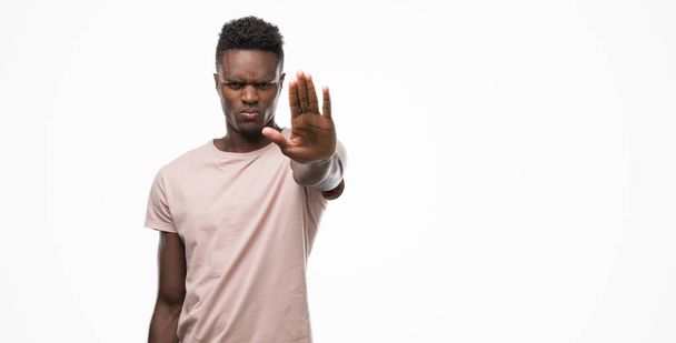Молодой африканский американец с открытой рукой делает знак стоп с серьезным и уверенным выражением, жест защиты
 - Фото, изображение