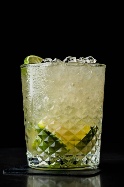 cold cocktail with lime and lemon. A glass of dew drops. Freshness, alcohol, bar. Black background - Fotó, kép
