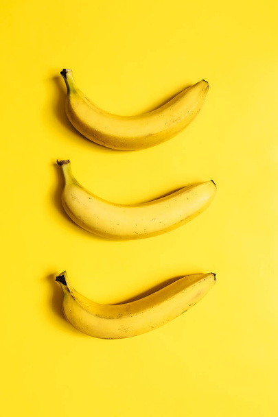Tree bananas on vibrant yellow background. Vertical composition. Minimalist concept. - Foto, imagen