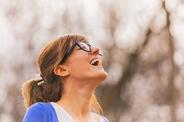 happy cute woman in eyeglasses smiling with closed eyes forest at sunny day - Photo, Image