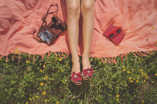 női lábak rózsaszín mintájú kamerával és foglaljon a napszemüveg-rét, sárga virágok  - Fotó, kép